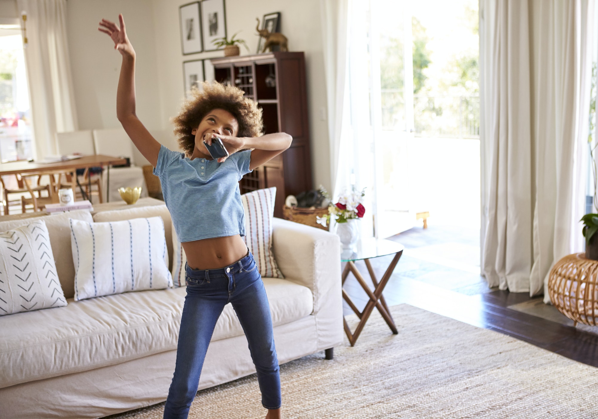 girl dancing and singing along to music in the living room at home